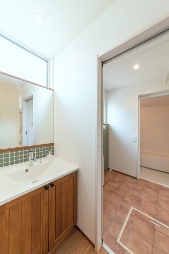 独立洗面の鏡下には、キッチンとカラーを合わせたモザイクタイルでアクセント。<br />
人工大理石のカウンターボウルに木の収納扉をかけあわせた洗面台は上品な印象に。<br />
使うたびに変化していく無垢の木の表情も楽しめます。<br />
